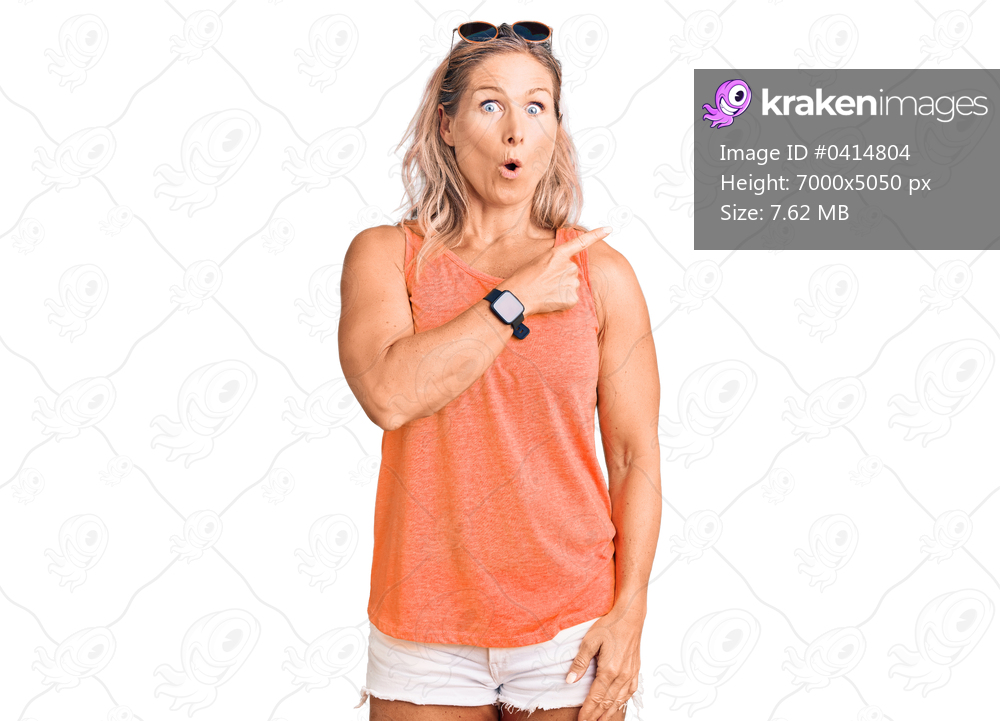 Middle age fit blonde woman wearing casual summer clothes and sunglasses surprised pointing with finger to the side, open mouth amazed expression. 
