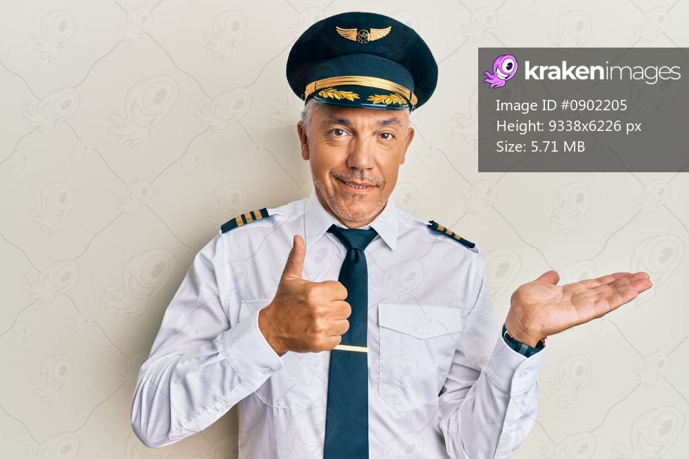 Handsome middle age mature man wearing airplane pilot uniform showing palm hand and doing ok gesture with thumbs up, smiling happy and cheerful 