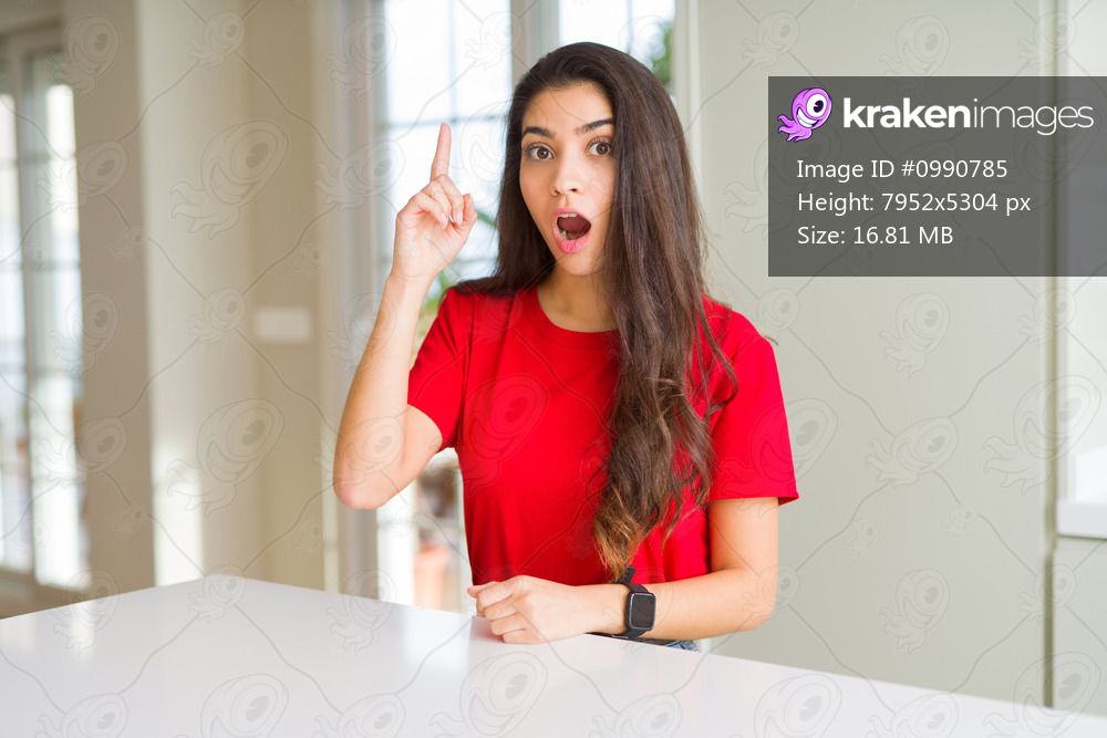 Young beautiful woman at home on white table pointing finger up with successful idea. Exited and happy. Number one.