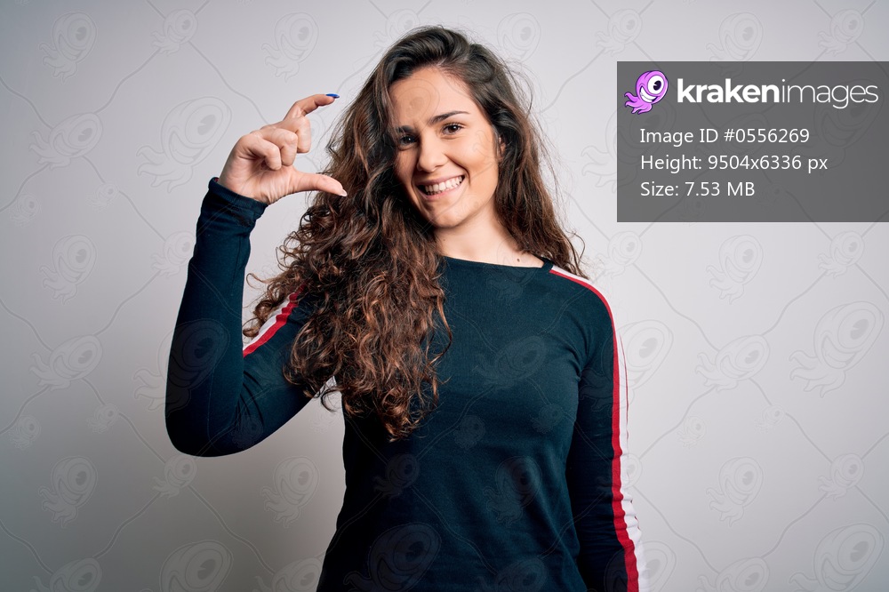 Young beautiful woman with curly hair wearing casual sweater over isolated white background smiling and confident gesturing with hand doing small size sign with fingers looking and the camera. Measure concept.