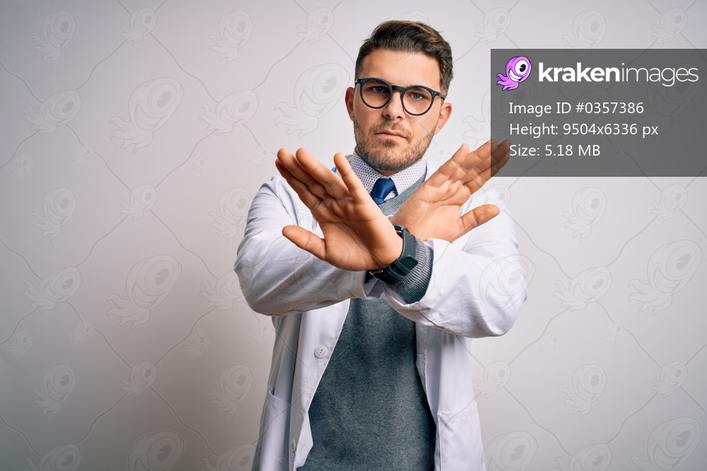Young doctor man with blue eyes wearing medical coat and stethoscope over isolated background Rejection expression crossing arms doing negative sign, angry face