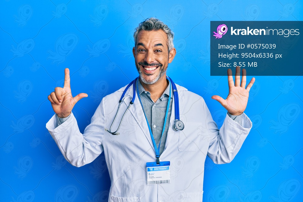 Middle age grey-haired man wearing doctor uniform and stethoscope showing and pointing up with fingers number seven while smiling confident and happy. 