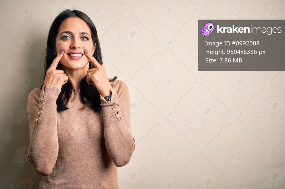 Young brunette woman with blue eyes wearing casual sweater over isolated white background Smiling with open mouth, fingers pointing and forcing cheerful smile