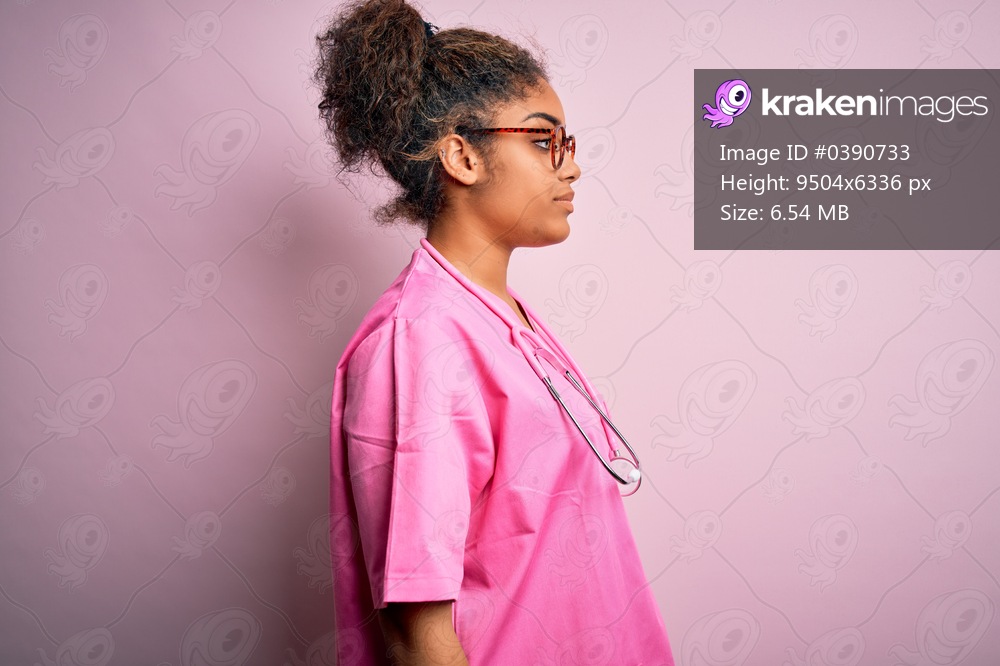 African american nurse girl wearing medical uniform and stethoscope over pink background looking to side, relax profile pose with natural face with confident smile.