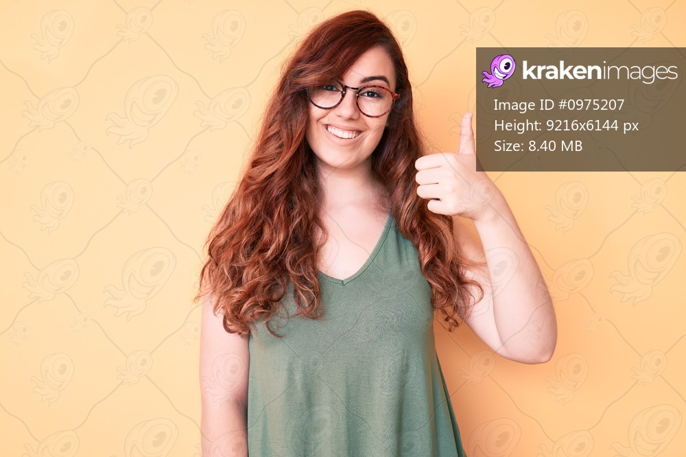 Young beautiful woman wearing casual clothes and glasses smiling happy and positive, thumb up doing excellent and approval sign 