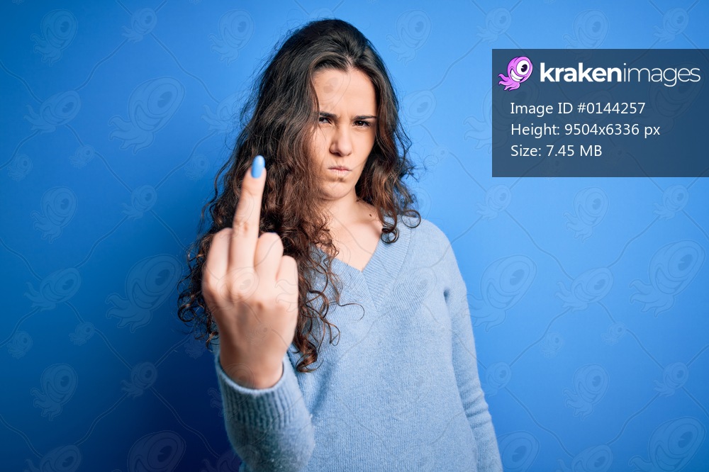 Young beautiful woman with curly hair wearing blue casual sweater over isolated background Showing middle finger, impolite and rude fuck off expression