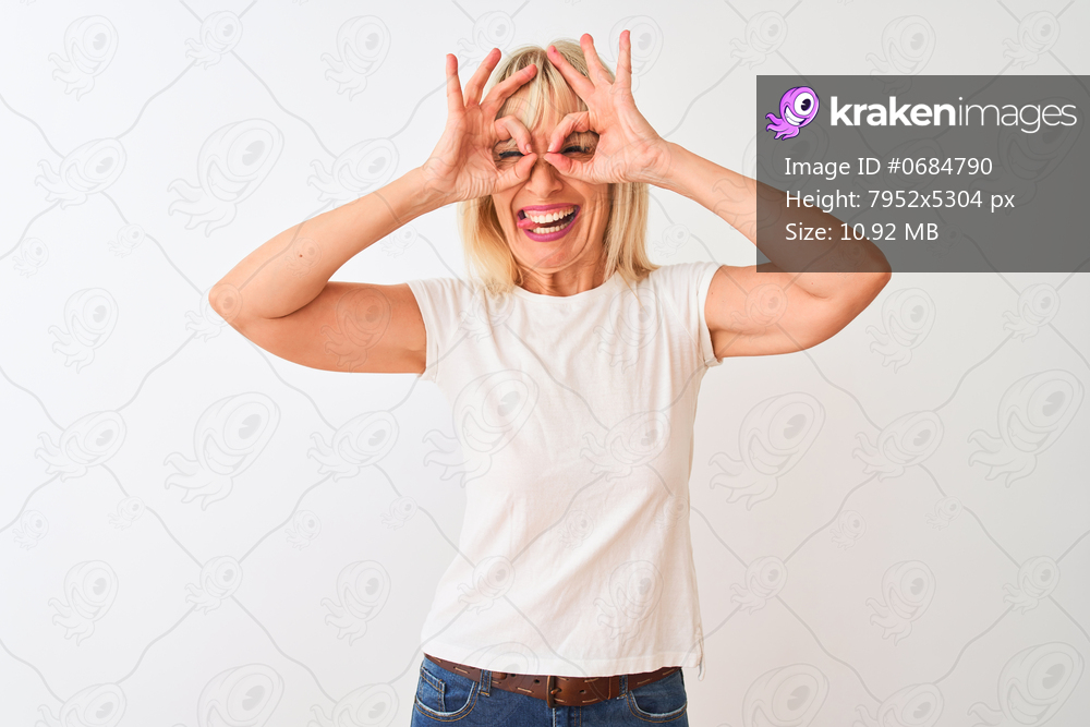 Middle age woman wearing casual t-shirt standing over isolated white background doing ok gesture like binoculars sticking tongue out, eyes looking through fingers. Crazy expression.