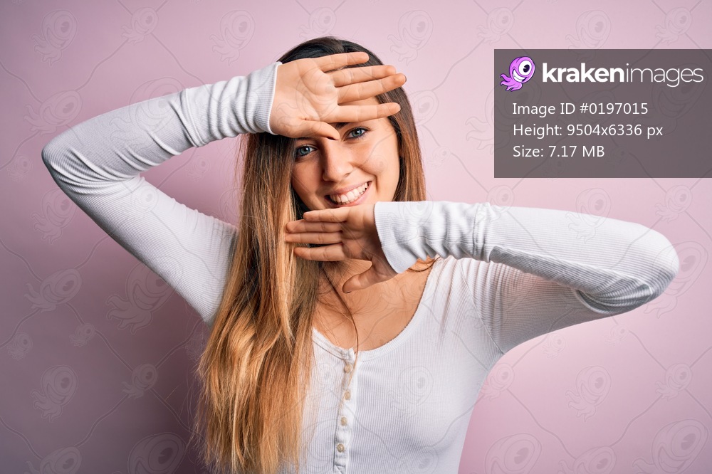 Young beautiful blonde woman with blue eyes wearing white t-shirt over pink background Smiling cheerful playing peek a boo with hands showing face. Surprised and exited
