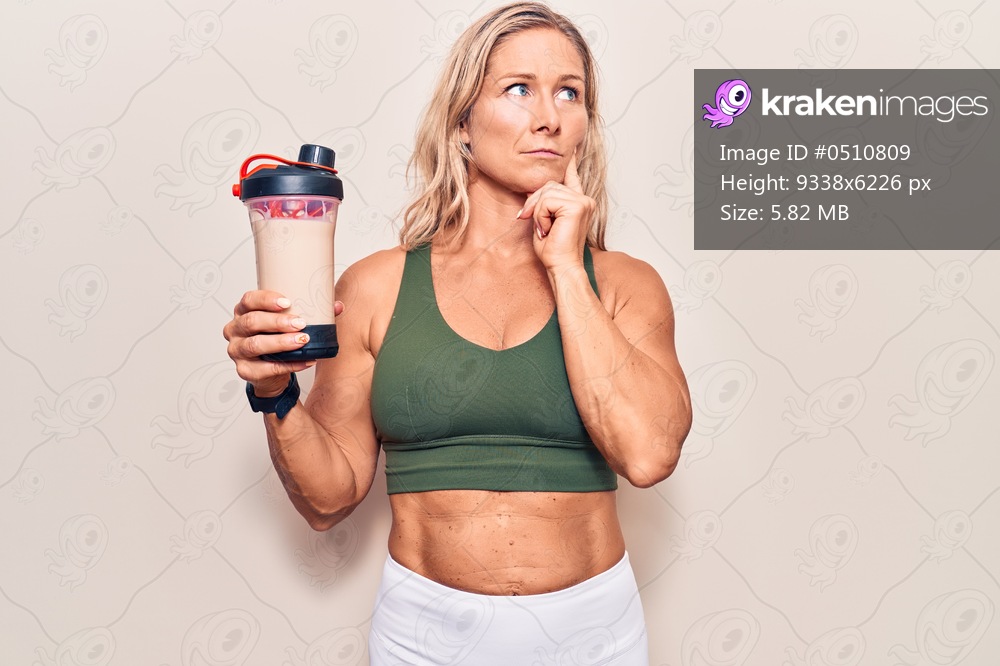 Middle age caucasian blonde woman wearing sport clothes drinking a protein shake serious face thinking about question with hand on chin, thoughtful about confusing idea 