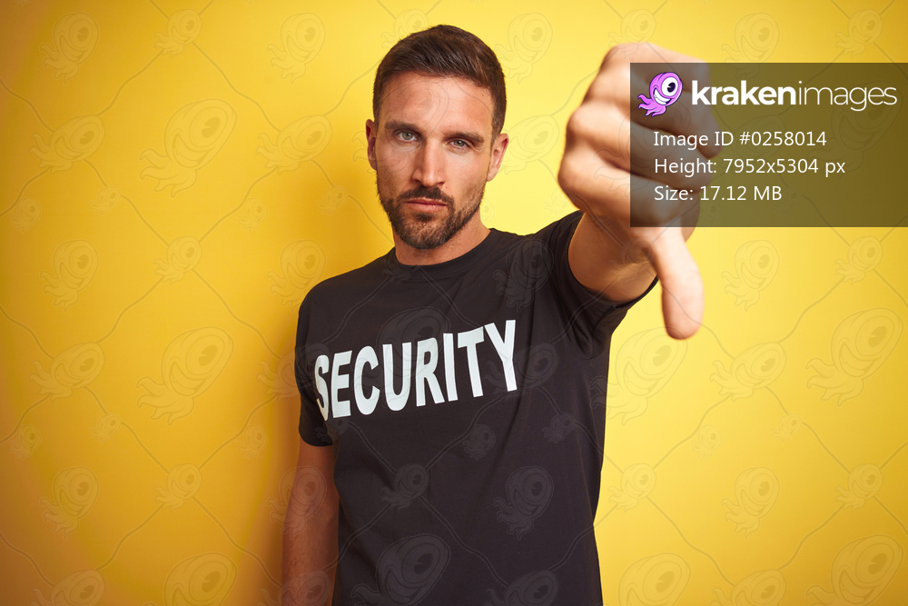 Young safeguard man wearing security uniform over yellow isolated background looking unhappy and angry showing rejection and negative with thumbs down gesture. Bad expression.