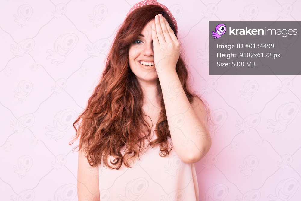 Young beautiful woman wearing casual clothes covering one eye with hand, confident smile on face and surprise emotion. 