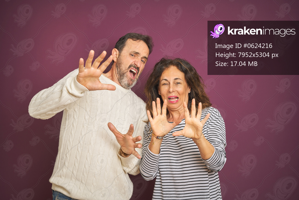 Beautiful middle age couple wearing winter sweater over isolated purple background afraid and terrified with fear expression stop gesture with hands, shouting in shock. Panic concept.