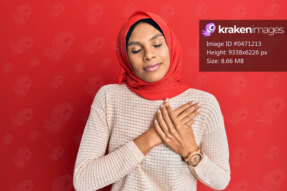 Young african american woman wearing traditional islamic hijab scarf smiling with hands on chest, eyes closed with grateful gesture on face. health concept. 