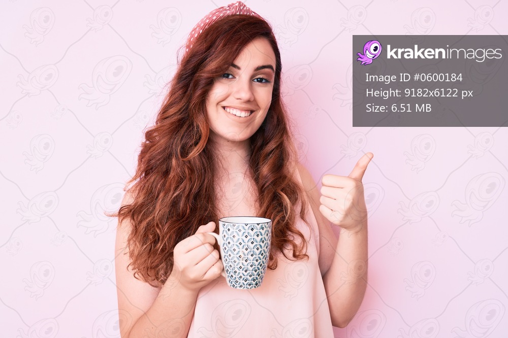 Young beautiful woman holding coffee smiling happy and positive, thumb up doing excellent and approval sign 
