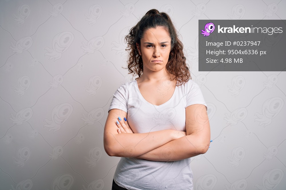 Young beautiful woman with curly hair wearing casual t-shirt standing over white background skeptic and nervous, disapproving expression on face with crossed arms. Negative person.