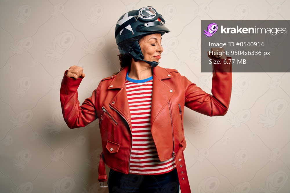 Middle age motorcyclist woman wearing motorcycle helmet and jacket over white background showing arms muscles smiling proud. Fitness concept.