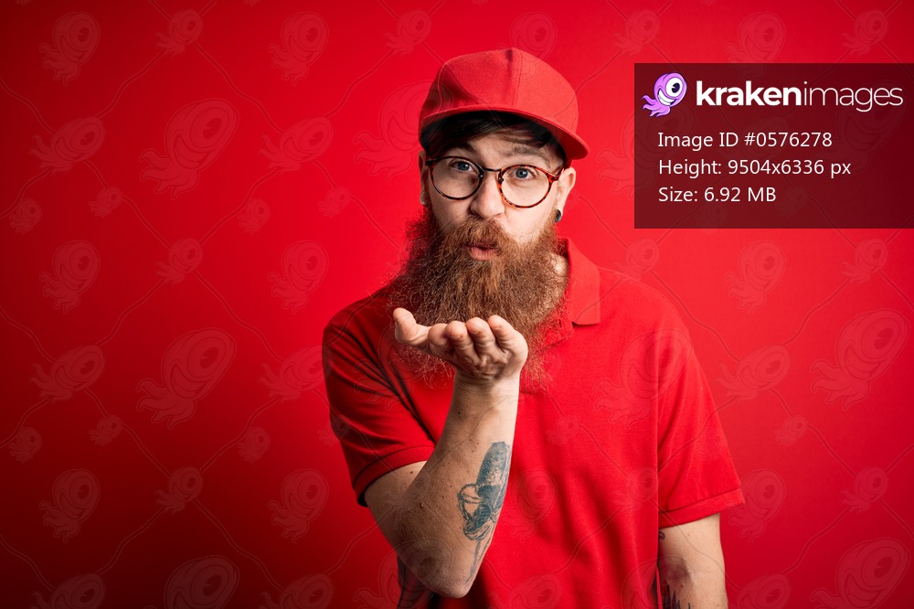 Young handsome delivery man wearing glasses and red cap over isolated background looking at the camera blowing a kiss with hand on air being lovely and sexy. Love expression.