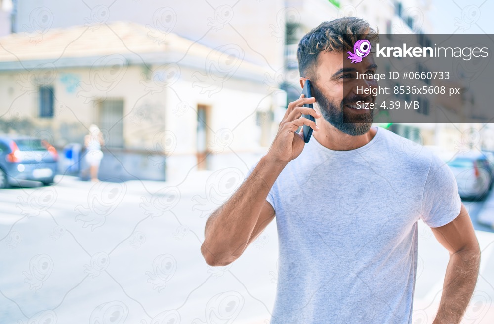 Young hispanic man smiling happy using smartphone walking at the cit