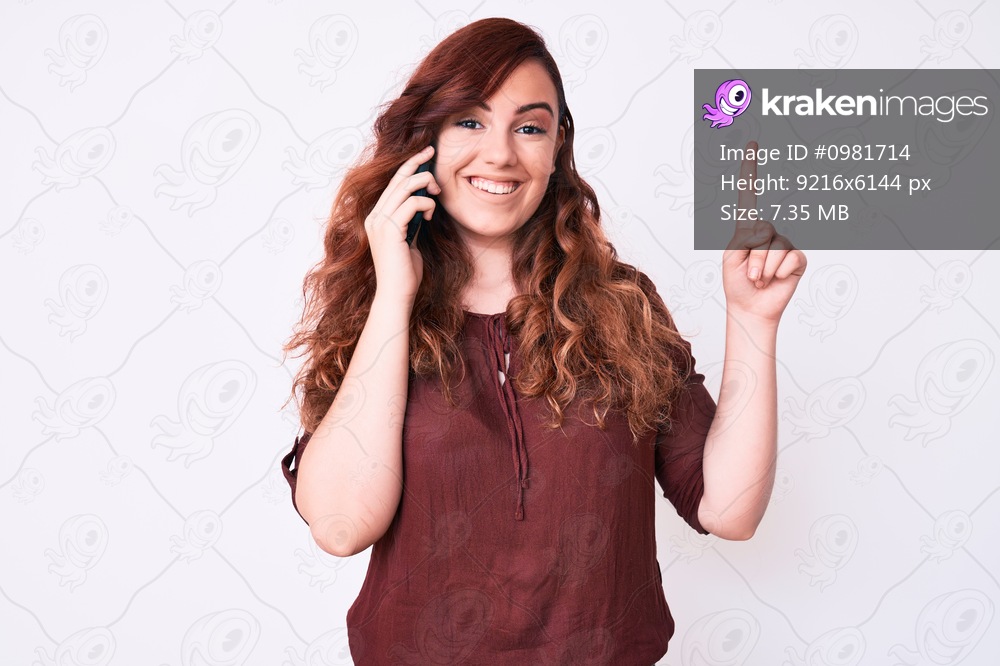 Young beautiful woman having conversation talking on the smartphone surprised with an idea or question pointing finger with happy face, number one 