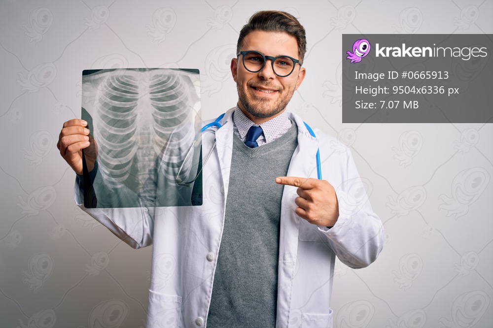 Young doctor man wearing medical coat looking at chest scan radiography over isolated background with surprise face pointing finger to himself