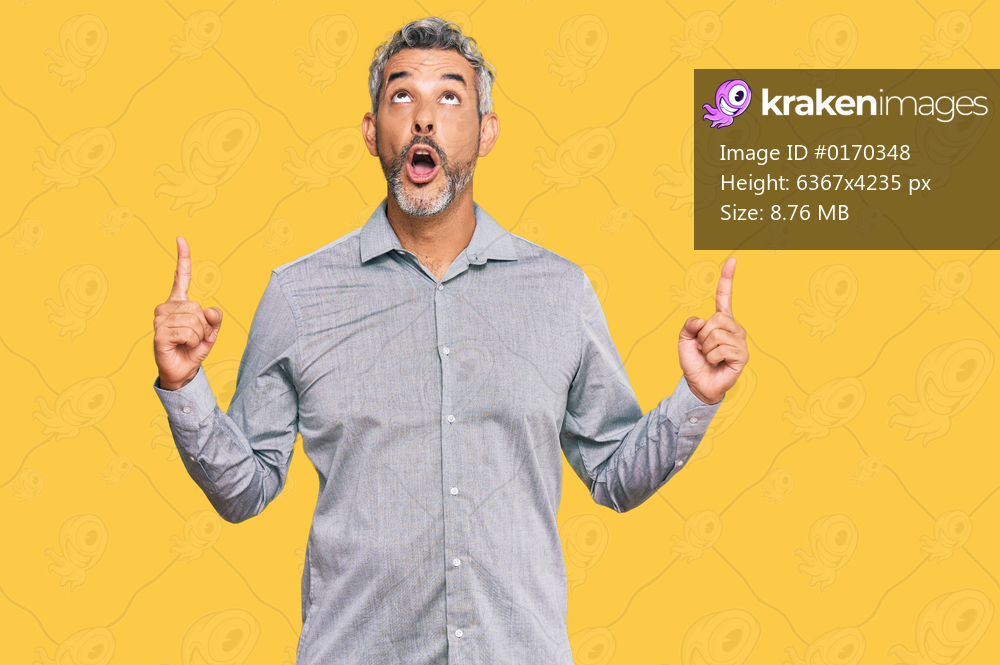 Middle age grey-haired man wearing casual clothes amazed and surprised looking up and pointing with fingers and raised arms. 