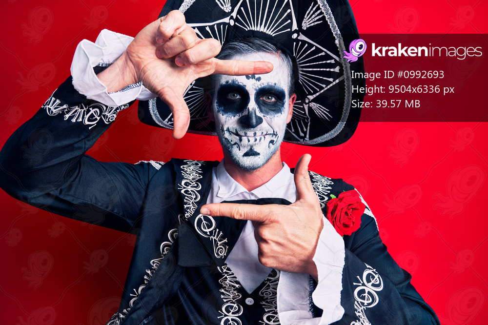 Young man wearing mexican day of the dead costume over red smiling making frame with hands and fingers with happy face. creativity and photography concept. 