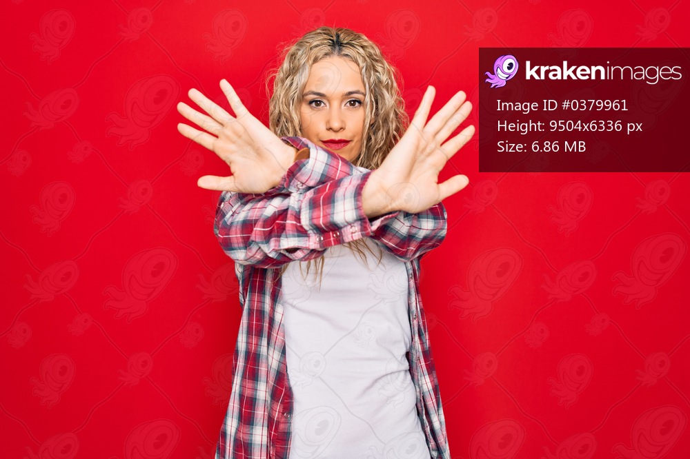 Young beautiful blonde woman wearing casual shirt standing over isolated red background Rejection expression crossing arms and palms doing negative sign, angry face