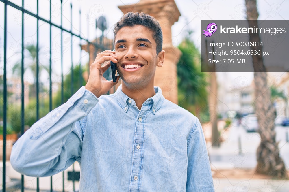 Young latin man smiling happy talking on the smartphone walking at the city.