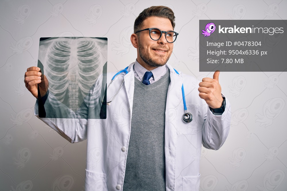 Young doctor man wearing medical coat looking at chest scan radiography over isolated background pointing and showing with thumb up to the side with happy face smiling