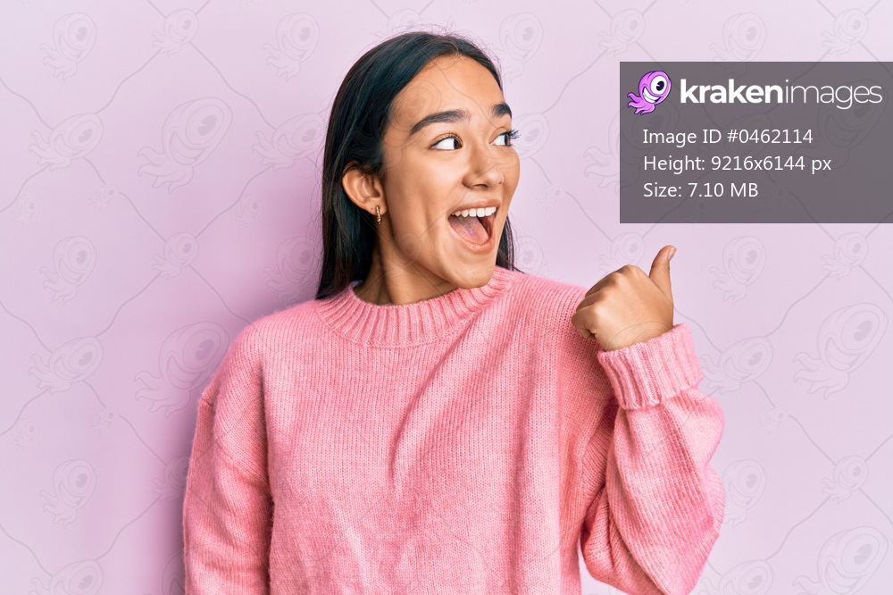 Young asian woman wearing casual winter sweater pointing thumb up to the side smiling happy with open mouth 