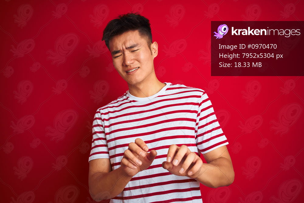 Young asian chinese man wearing striped t-shirt standing over isolated red background disgusted expression, displeased and fearful doing disgust face because aversion reaction. With hands raised. Annoying concept.