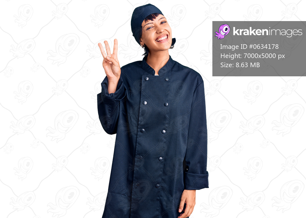 Young brunette woman with short hair wearing professional cook uniform showing and pointing up with fingers number three while smiling confident and happy. 