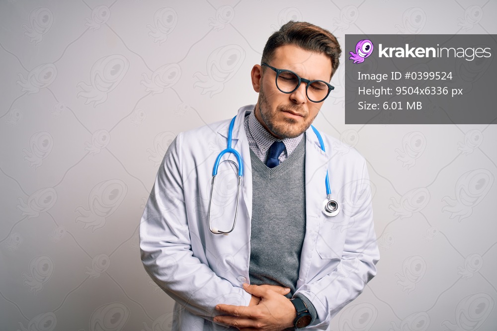 Young doctor man with blue eyes wearing medical coat and stethoscope over isolated background with hand on stomach because indigestion, painful illness feeling unwell. Ache concept.