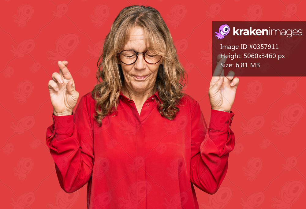 Middle age blonde woman wearing casual shirt over red background gesturing finger crossed smiling with hope and eyes closed. luck and superstitious concept. 