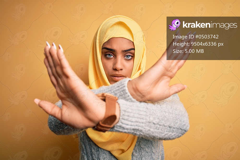 Young beautiful african american girl wearing muslim hijab over isolated yellow background Rejection expression crossing arms and palms doing negative sign, angry face