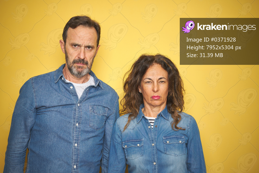 Beautiful middle age couple together standing over isolated yellow background skeptic and nervous, frowning upset because of problem. Negative person.
