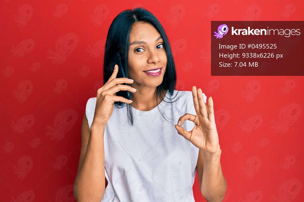 Young african american woman having conversation talking on the smartphone doing ok sign with fingers, smiling friendly gesturing excellent symbol 