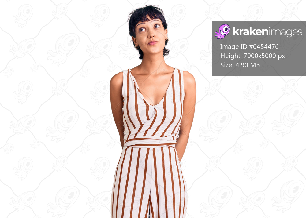 Young brunette woman with short hair wearing summer outfit smiling looking to the side and staring away thinking. 