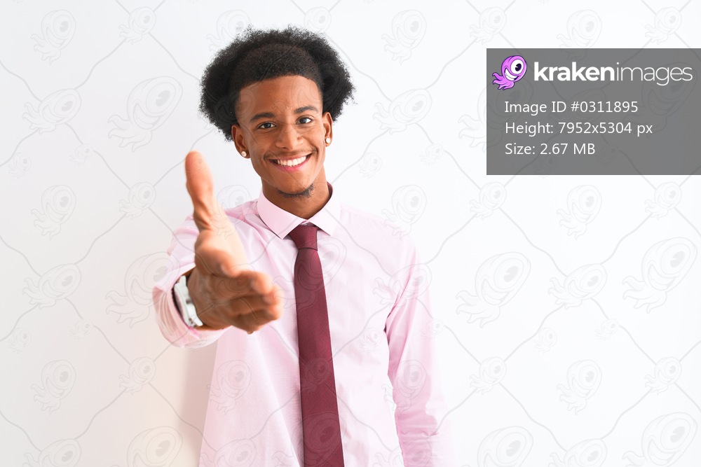 Young african american businessman wearing tie standing over isolated white background smiling friendly offering handshake as greeting and welcoming. Successful business.