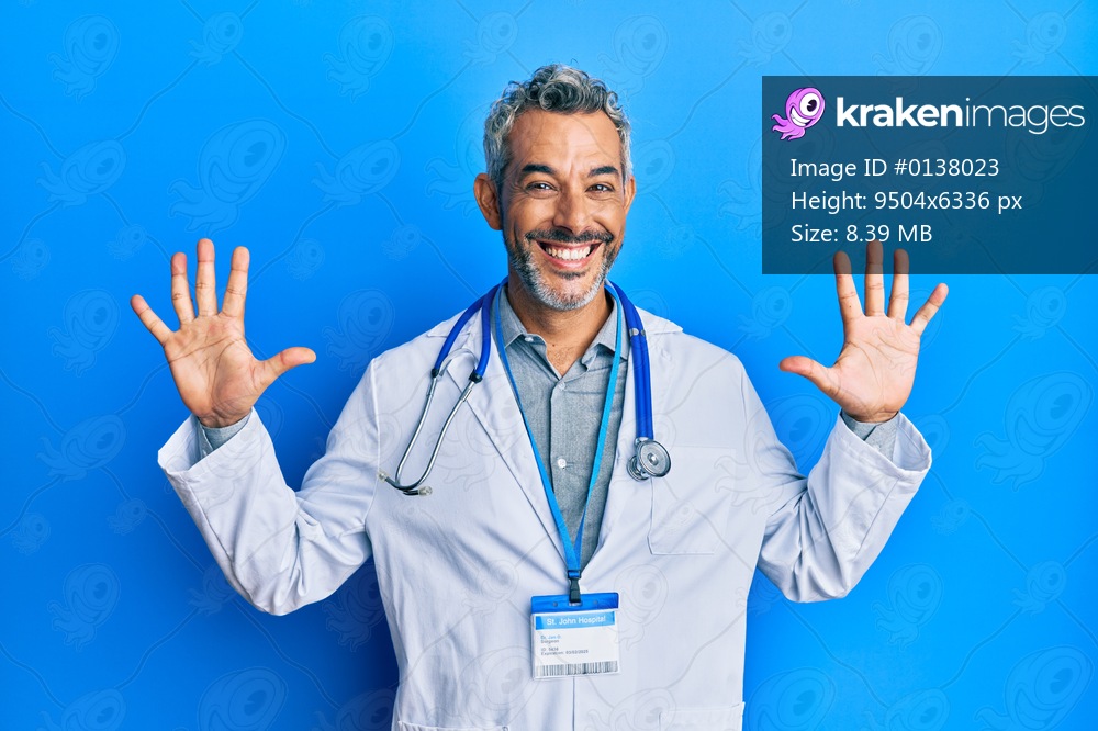 Middle age grey-haired man wearing doctor uniform and stethoscope showing and pointing up with fingers number ten while smiling confident and happy. 