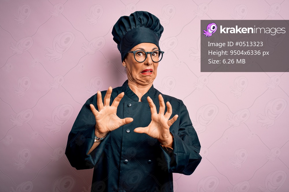 Middle age brunette chef woman wearing cooker uniform and hat over isolated pink background afraid and terrified with fear expression stop gesture with hands, shouting in shock. Panic concept.