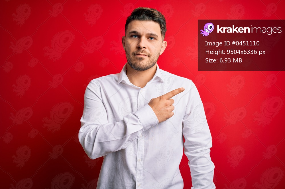 Young business man with blue eyes wearing elegant shirt standing over red isolated background Pointing with hand finger to the side showing advertisement, serious and calm face