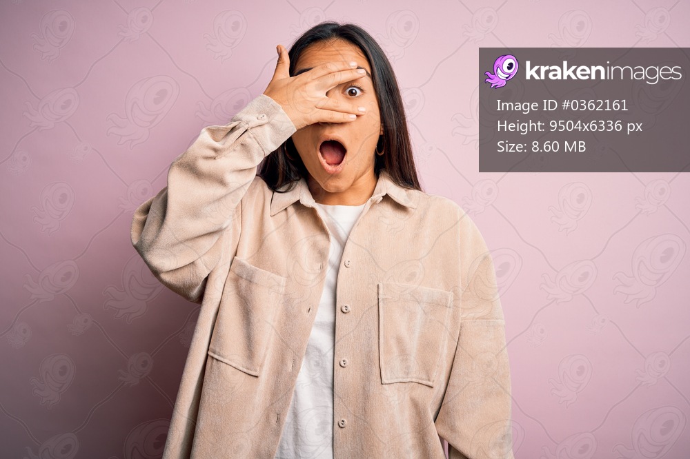 Young beautiful asian woman wearing casual shirt standing over pink background peeking in shock covering face and eyes with hand, looking through fingers with embarrassed expression.