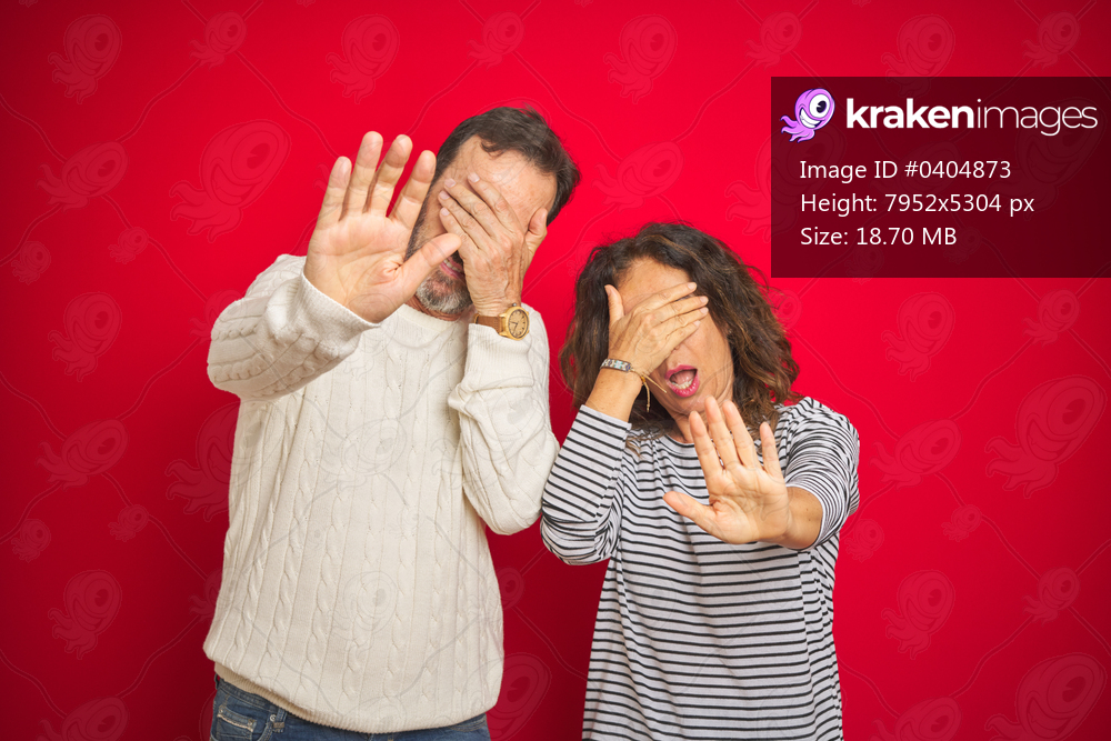 Beautiful middle age couple wearing winter sweater over isolated red background covering eyes with hands and doing stop gesture with sad and fear expression. Embarrassed and negative concept.