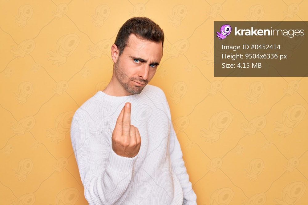 Young handsome man with blue eyes wearing casual sweater standing over yellow background Beckoning come here gesture with hand inviting welcoming happy and smiling