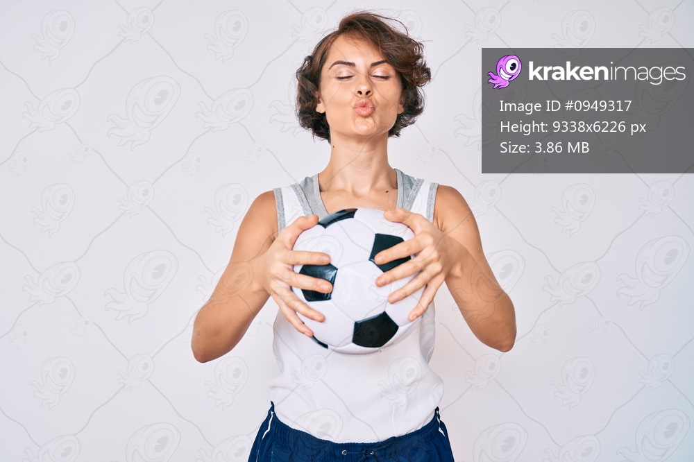 Young hispanic woman holding soccer ball looking at the camera blowing a kiss being lovely and sexy. love expression. 