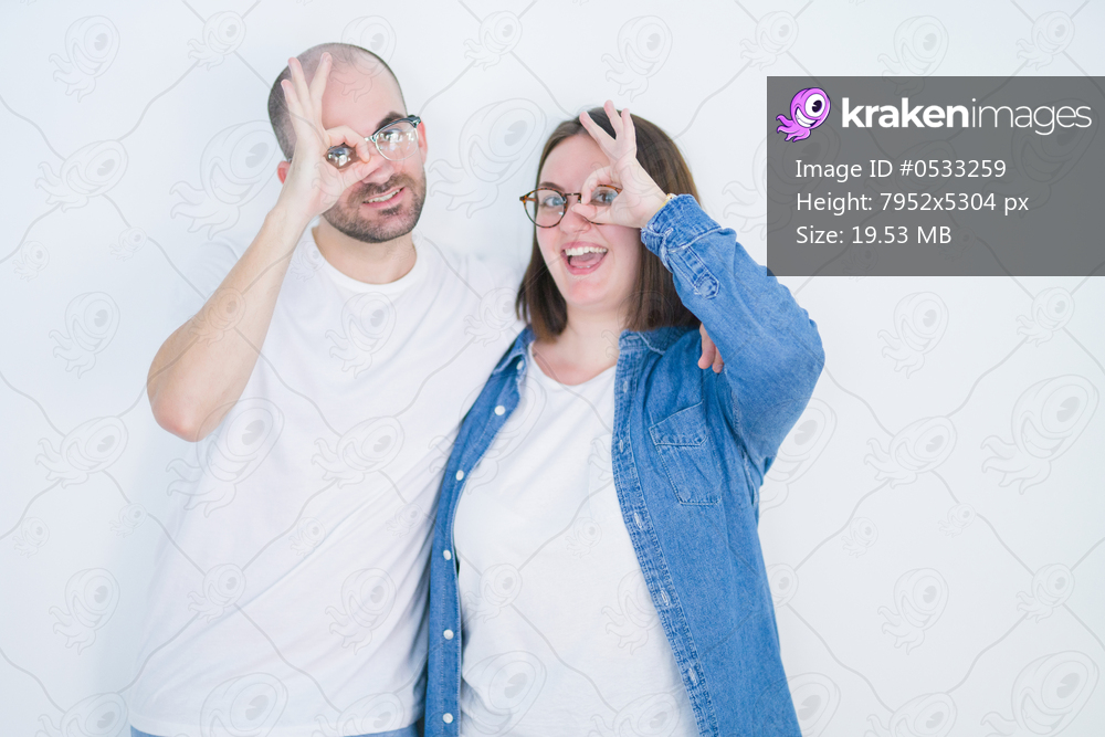 Young couple together wearing glasses over white isolated background with happy face smiling doing ok sign with hand on eye looking through fingers