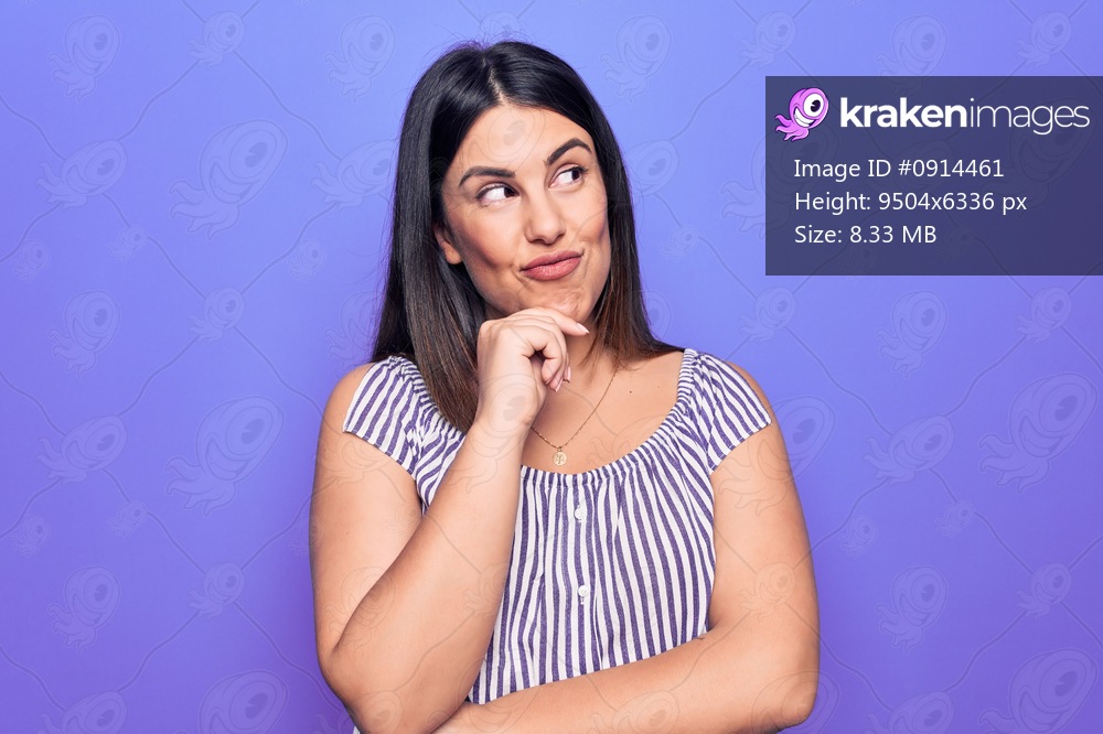 Young beautiful brunette woman wearing casual striped t-shirt standing over purple background thinking concentrated about doubt with finger on chin and looking up wondering