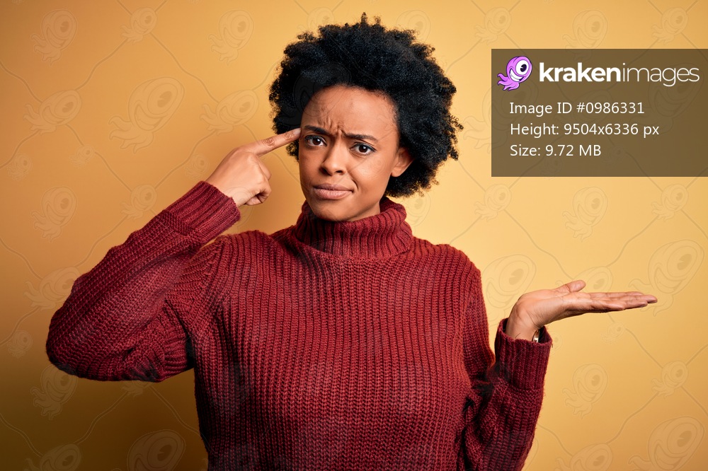 Young beautiful African American afro woman with curly hair wearing casual turtleneck sweater confused and annoyed with open palm showing copy space and pointing finger to forehead. Think about it.
