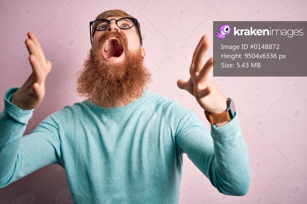 Handsome Irish redhead man with beard wearing glasses over pink isolated background crazy and mad shouting and yelling with aggressive expression and arms raised. Frustration concept.